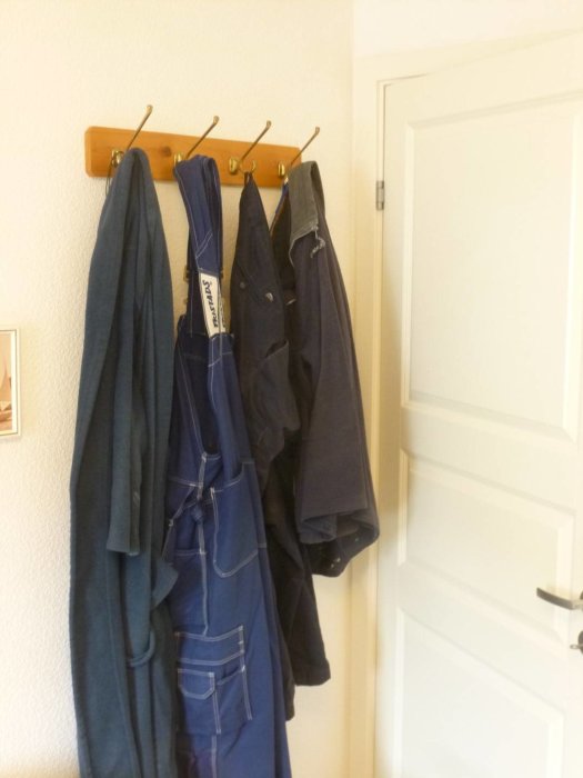 Klädhook med jackor och arbetskläder hängande intill en stängd vit dörr.
