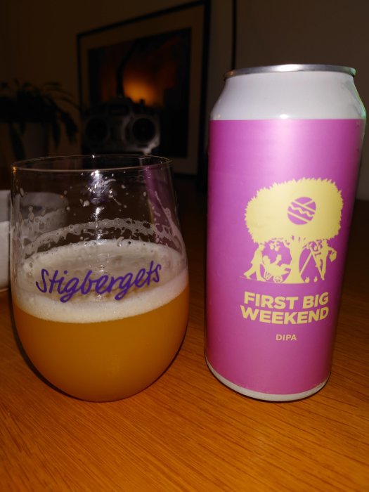 Ölglas märkt "Stigbergets" med hälften kvar av en gyllene dryck, bredvid en lila burk "FIRST BIG WEEKEND DIPA".