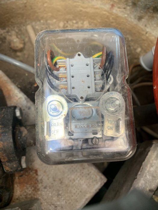 Kopplingsdosa med texterna "till" och "från" på metallbrickor, kablar och elektrisk komponent inuti.