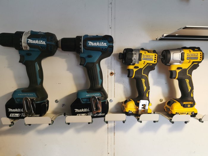 Fyra elektriska skruvdragare upphängda på väggfästen, två Makita och två DeWalt, ordnade i jämn rad.