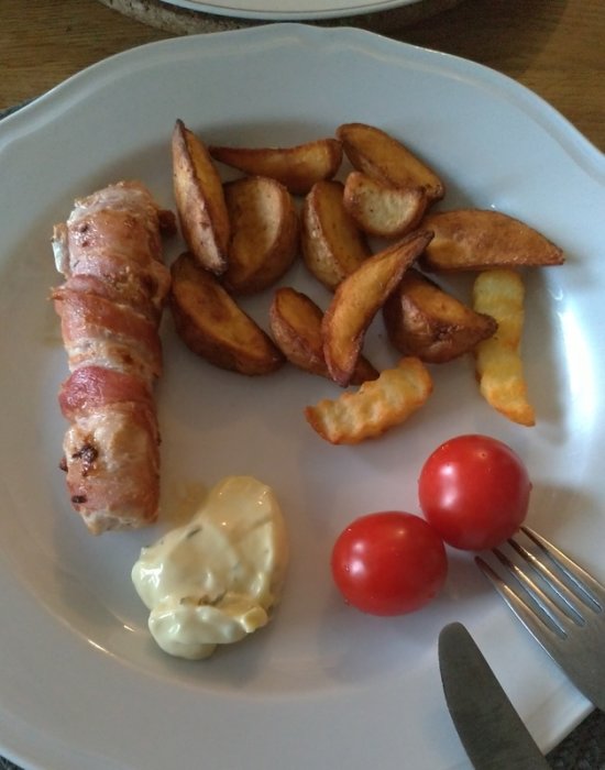 Baconlindad kycklingfilé med klyftpotatis, tomater och sås på en tallrik.