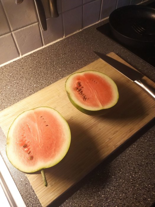Halverad vattenmelon på skärbräda med kökskniv vid sidan.