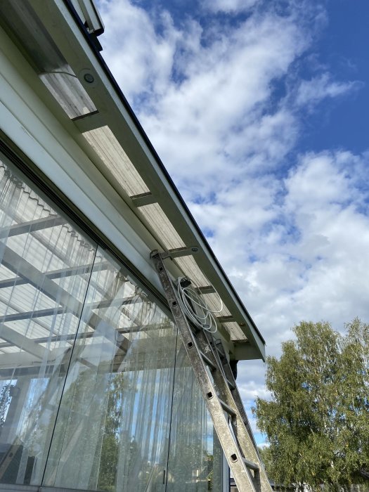 Montering av grundmålat virke och spotlights på utsidan av ett glastak, med en stege lutad mot huset.