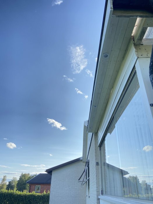 Nyinstallerade takspottar på vitmålat virke under takutskjut på hus med blå himmel i bakgrunden.