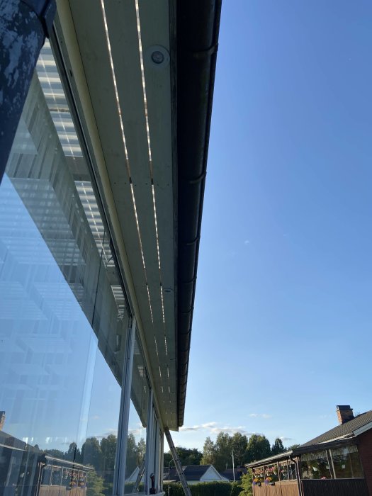 Utsikt under takfot med grundmålat virke och integrerade spottar mot en klarblå himmel.