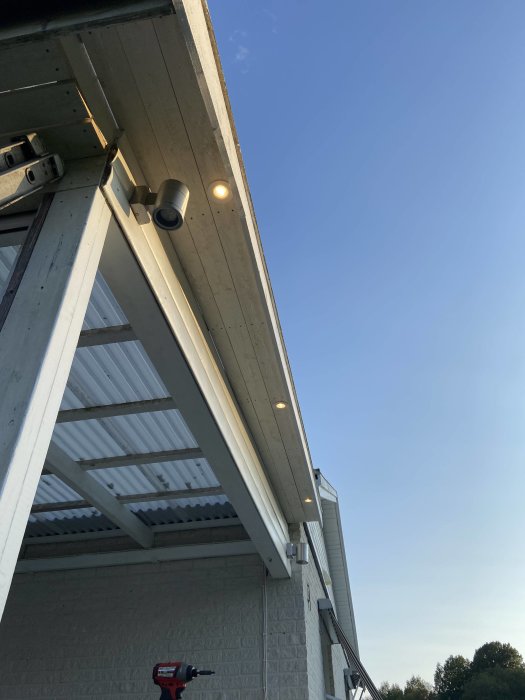 Montering av spottar på grundmålat virke längs husets taköverhäng mot en klarblå himmel.