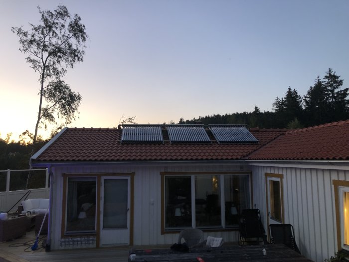 Solfångare installerade på ett tegelrött tak av ett hus vid skymning.