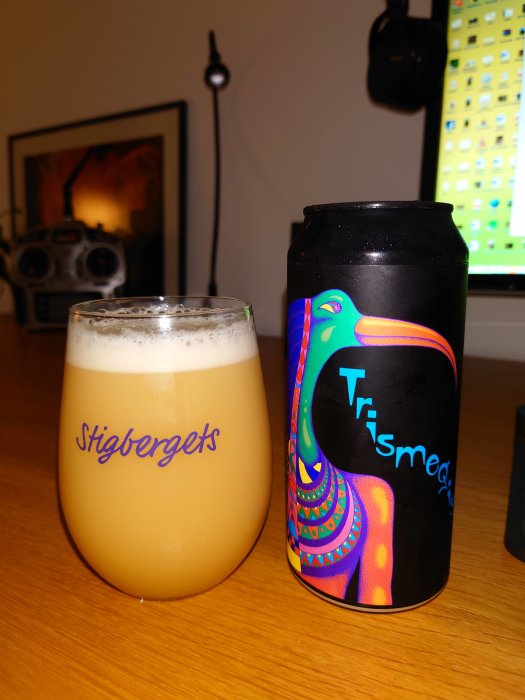 Ölglas märkt "Stigbergets" och burk med färgglad tukan design, "Trismegistos" på en bordsyta.