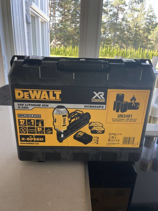 DeWalt verktygslåda med bild av borrmaskin och batterier, placerad inomhus bredvid ett fönster.