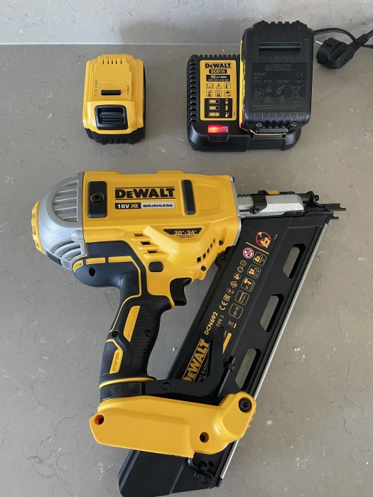 DeWalt spikpistol och två uppladdningsbara batterier på en betongyta, som gestaltning av märkesbyte.