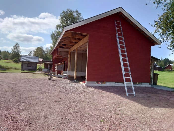 Nybyggd rödfärgad lada med oavslutad snickarbod och stege längs väggen under en klar himmel.