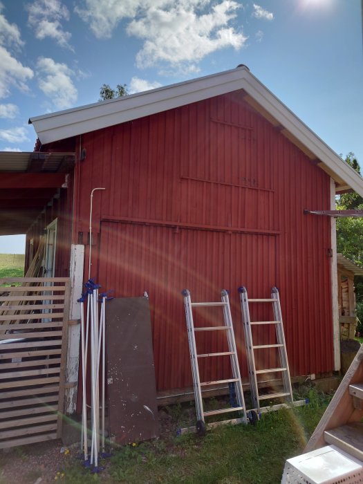 Ny målade röda vindskivor på en träfasad med stegar lutade mot husväggen.