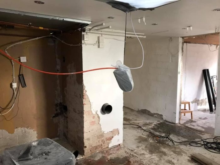 Renoveringsarbete i ett tomt rum med borttaget tak och väggbeklädnad, exponerade kablar och byggavfall.