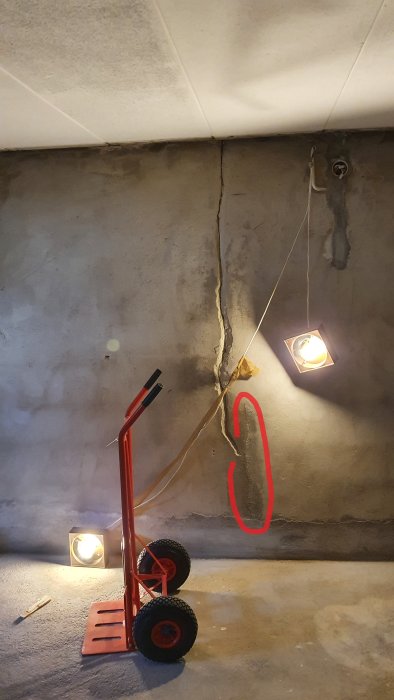 En källarvägg med en stor spricka markerad med rött där tidigare lagning vittrat sönder, med golvvagn i förgrunden.