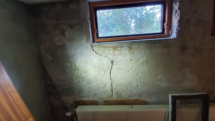 Källarvägg med spricka under fönstret, avrådd puts och synlig tidigare reparation.