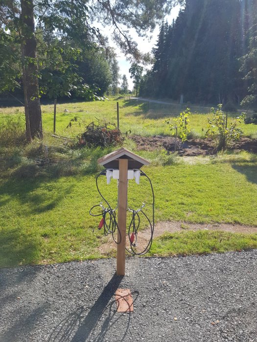 Nybyggd stolpe för motorvärmare med tak och elkontakter på en solig gräsmatta.