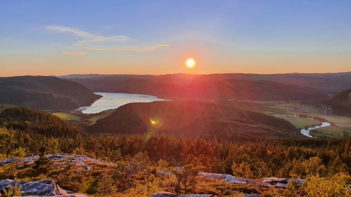 Solnedgång över ett bergslandskap med en flod och skog.