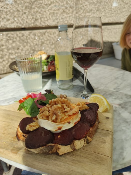 Njutning vid uteservering med en bricka med brieost, rödbetor och valnötter på bröd, sida om sida med ett glas vin och limonad.