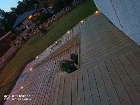 Nybyggd träterrass med integrerad belysning vid skymning, omgiven av en lummig trädgård.