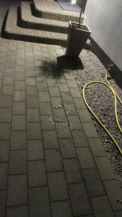 Slemmönster i intervaller på plattläggning vid trappsteg och kruka med gul slang.