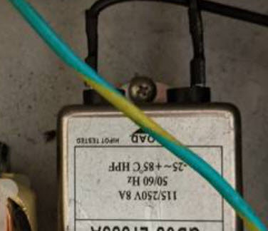 Skruv på ett elektroniskt apparats chassi med etikett och ledning i förgrunden.