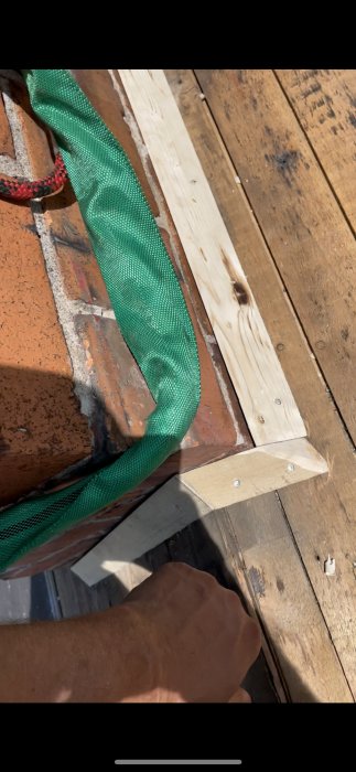 Närbild på tak med trälist och grön spännrem runt en tegelskorsten under arbete.