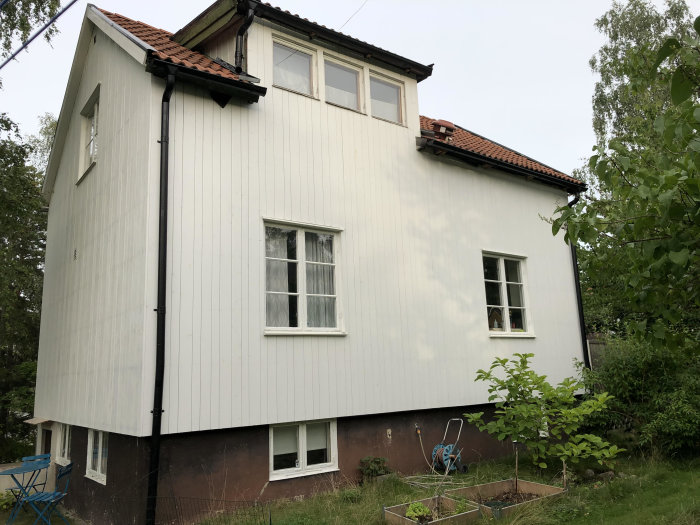 Vitmålat hus från 1930-talet med två våningar och varierande fönster, omgivet av grönska.