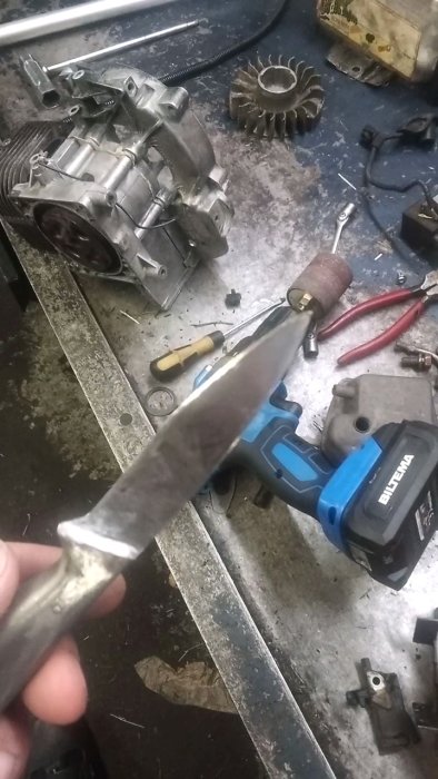 Svetsad och reparerad fruktkniv hålls upp i en verkstad med verktyg och maskindelar i bakgrunden.