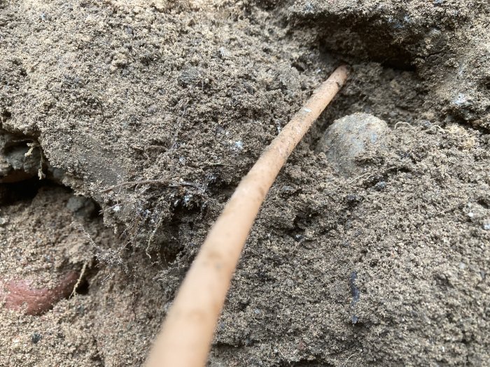 En tunn orangefärgad slang syns på en byggarbetsplats, halvt dold i sand och grus nära en betonggrund.