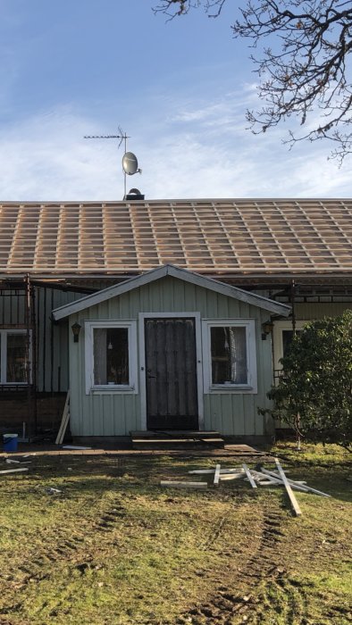 Farstun på ett hus med nymålat träfasad och nytt tak, byggmaterial framför byggnaden.