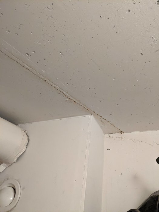 Sprickor i taket och längs hörnet av en vägg i en klädkammare, tecken på tidigare spacklingsförsök.