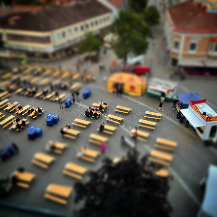 Oskarp bild av ett torg med människor och marknadsstånd, tilt-shift-effekt ger miniatyrytseende.
