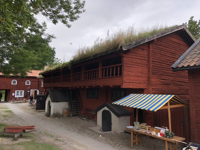 Traditionellt rött trähus med grästak, balkong och markis i historisk miljö.