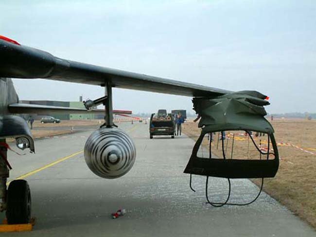 Damaged airplane wing with detached engine parts on a runway.