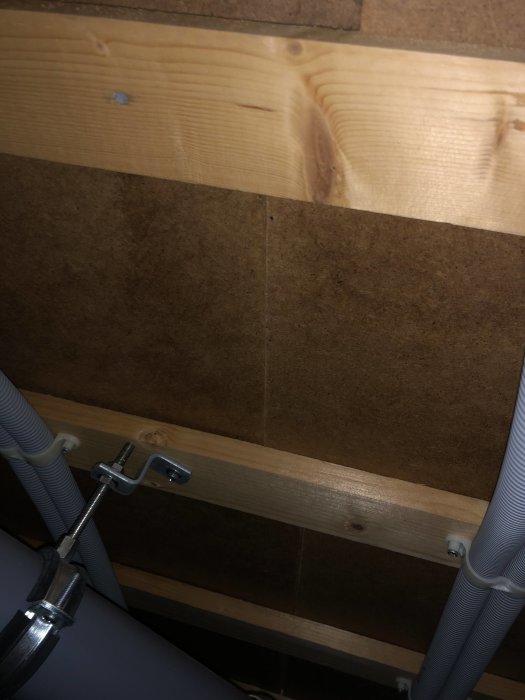 Fuktmärken på bottenskiva i byggprojekt, synliga mellan träreglar och rörinstallationer.