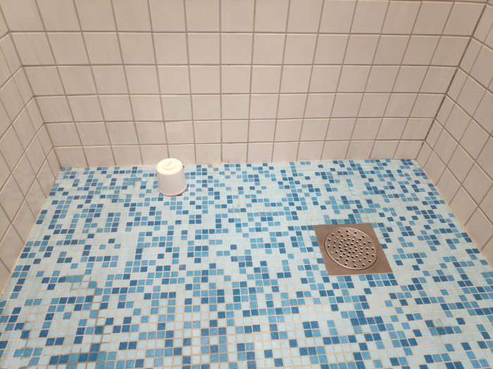 Mosaikbelagt badrumsgolv med avloppsrör och golvbrunn som eventuellt hindrar installation av badkar.
