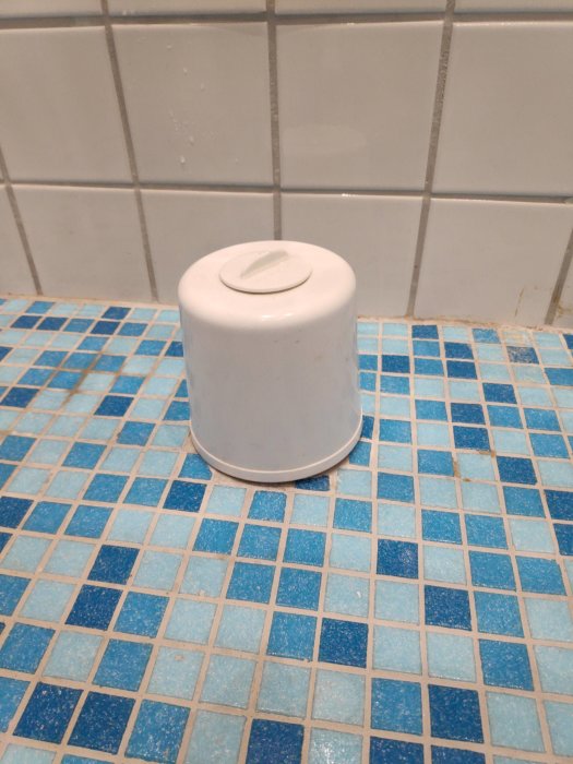 Avloppsrör med lock på ett blått och vitt kaklat badrumsgolv, potentiellt i vägen för nytt badkar.