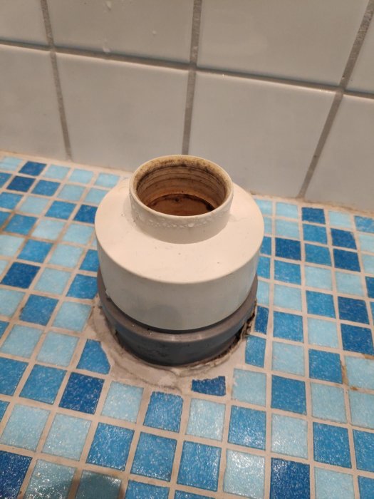 Ett badrumsgolv med blå och vita kakelplattor och ett synligt avloppsrör som utgör ett hinder för installation.