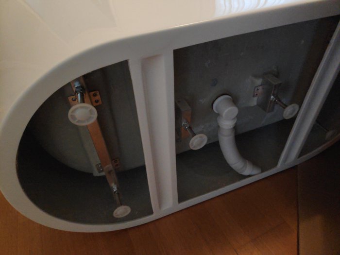 Undersidan av ett badkar som visar avloppsröret i vägen för stativets korssträva.