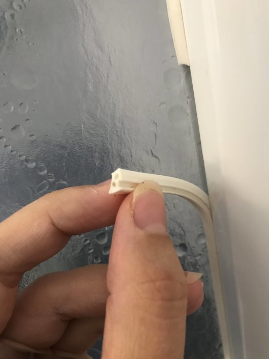 En hand som håller en vit, ovanlig profilformad list vid en duschvägg.