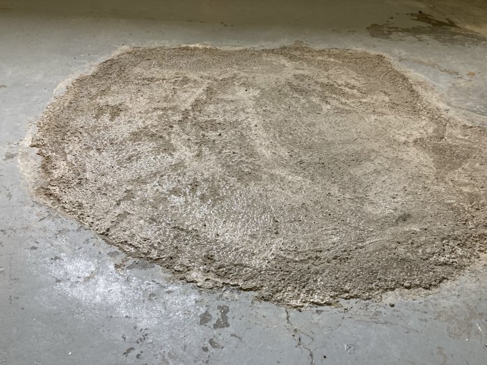 Nyigenlagt golvbrunnshål med finbetong i ett oinrett källarrum, ytan är ojämn och grov.