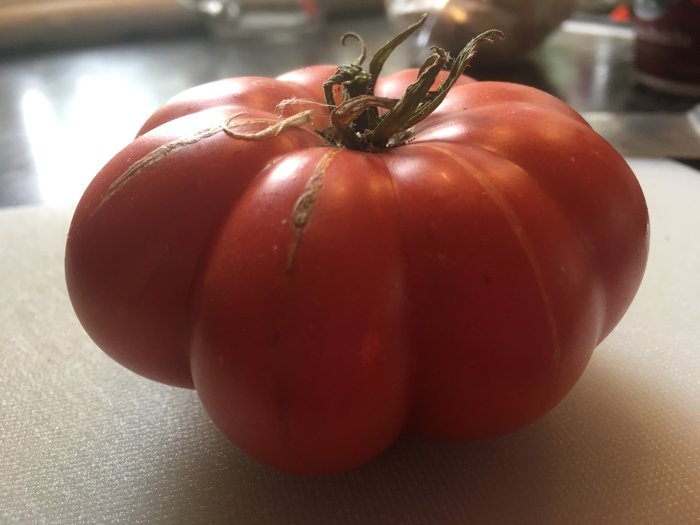 Mogen röd tomat med tydliga segment och stjälk, beskrivs som söt och lite mjuk inuti.