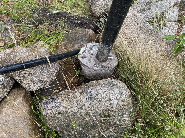 Stolplykta monterad på en betongklump bland stenar och gräs i behov av omgjutning.