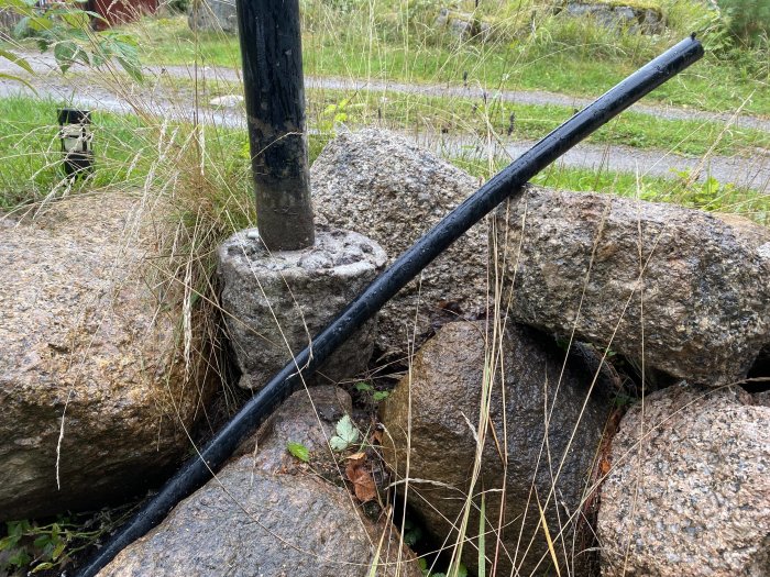 Stolplykta lutar mot stenar med gammal betongfundament vid sidan om gräs och löv.