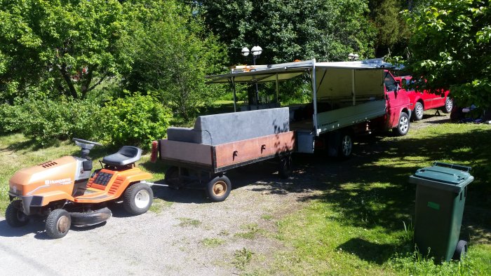 Husqvarna trädgårdstraktor kopplad till anpassad vagn i en solig trädgård.