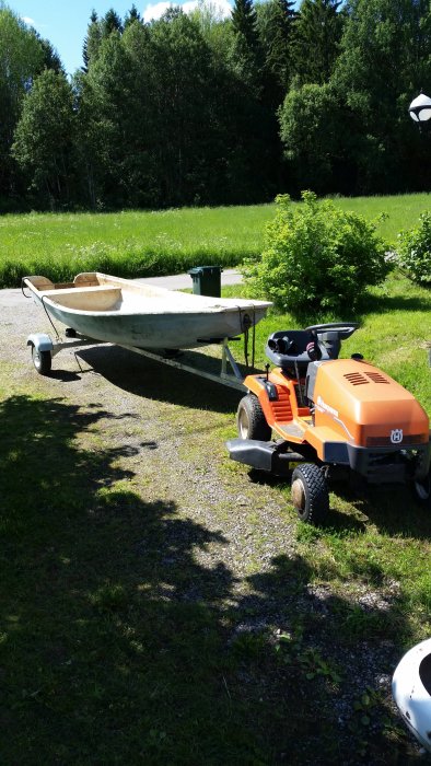 En Husqvarna trädgårdstraktor kopplad till en modifierad vagn med en båt, står i en solig trädgård.