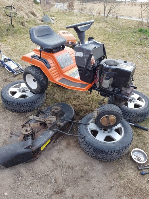 Gammal Husqvarna trädgårdstraktor demonterad under reparation med synliga motor- och klippdelskomponenter.