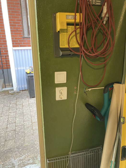 Elektrisk panel med omdragen kabel, nya brytare och uttag i ett garage med gröna väggar.