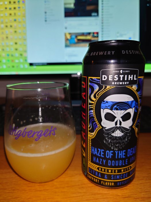 Ölglas delvis fyllt med öl framför en burk med texten "DESTIHL BREWERY HAZE OF THE DEAD" mot en datorskärm.