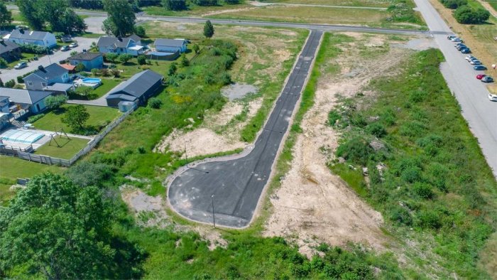 Flygbild av obebyggda tomter med markerade nummer längs en väg, intill befintliga hus.